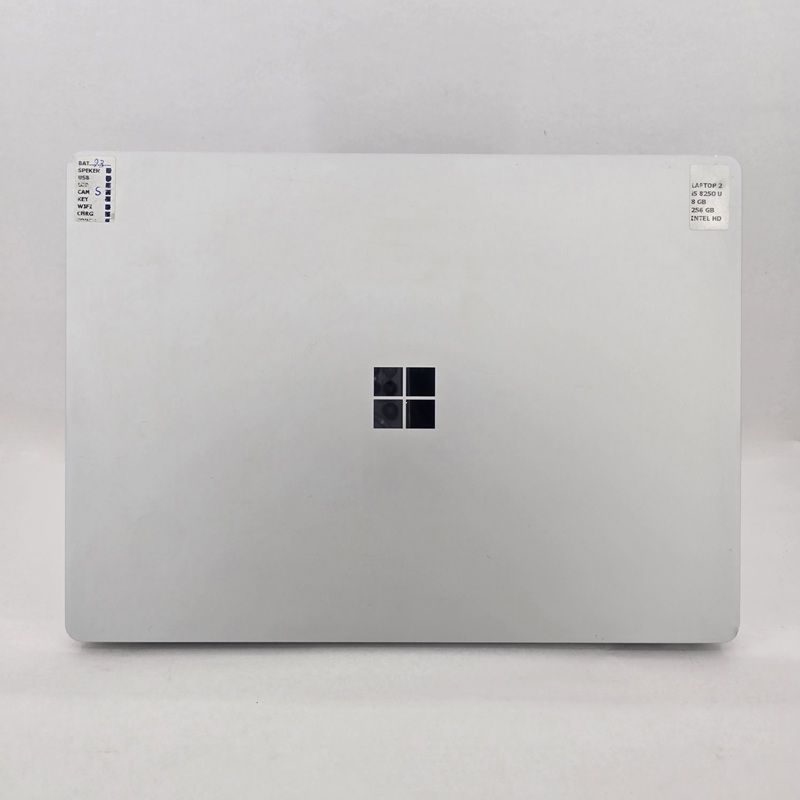 نمای پشت لپ تاپ استوک Microsoft Surface Laptop 2 با طراحی مینیمال و بدنه آلومینیومی صاف و براق، لوگوی مایکروسافت در مرکز، بدون پورت یا درگاه قابل مشاهده.